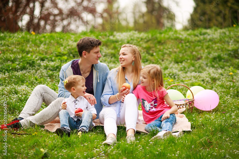 Fototapeta premium Happy family on picnic in flowered park sitting on grass, parenthood leisure in nature
