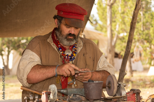 фотографія A man dressed as an 1800's tinker in a mountain man festival files the edge of a copper trinket he is making