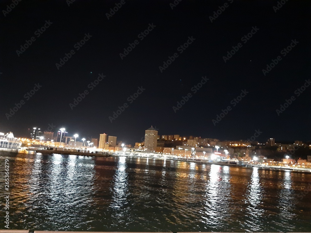 Genova, Italy - 04/19/2019: An amazing caption of the sea shore of Genoa by night in spring with some beautiful lights of the sheeps and a great view to a part of the city.