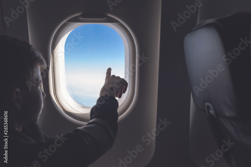 A boy have flight looking in the airplane window or porthole.
