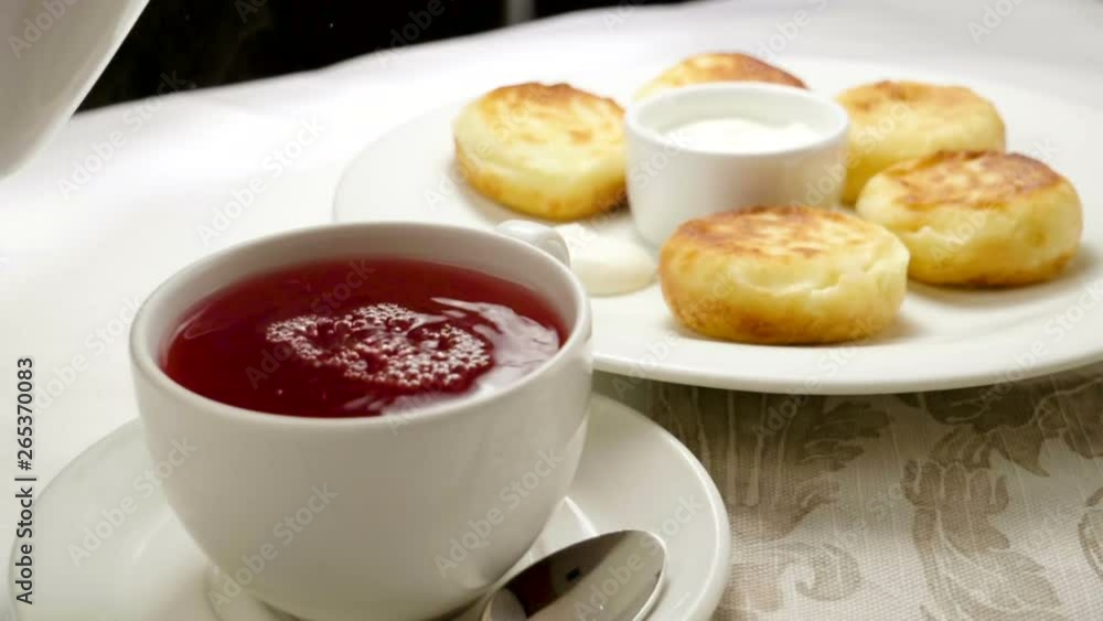Fruit tea is being poured into a cup on the background of a plate with cheesecakes. Slow motion. HD Fruit tea is being poured into a cup on the background of a plate with cheesecakes. Slow motion. HD