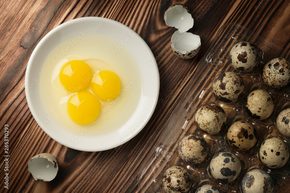 Top view yolks and whites of quail eggs in a plate and a plastic container with fresh eggs on a wooden table Top view yolks and whites of quail eggs in a plate and a plastic container with fresh eggs on a wooden table