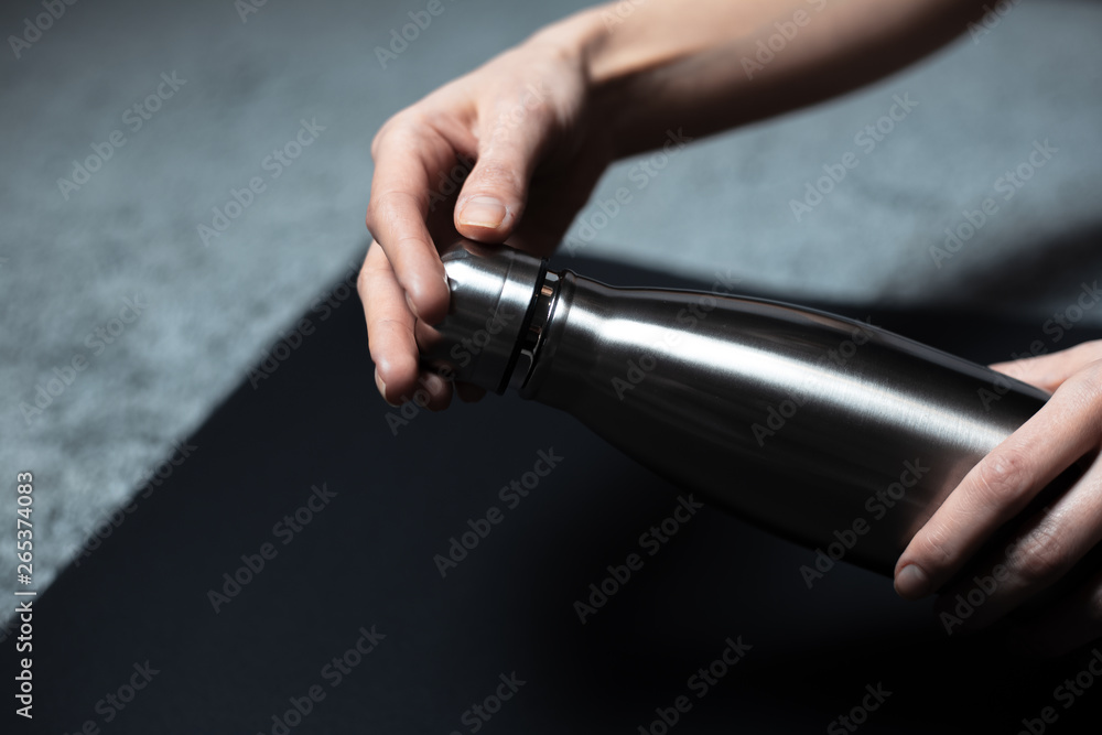 Close-up of hand holding ecologic steel thermo bottle for water, on black background