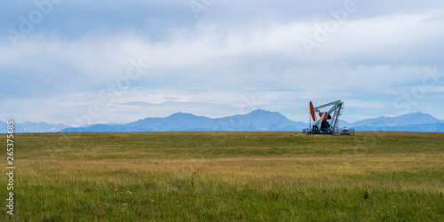 A pump jack at an oil well in a grass field with the Canadian Rocky mountains in the distance; Alberta, Canada