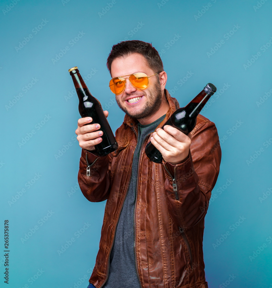 Photo of smiling man in orange glasses and leather jacket with two bottles in hands Photo of smiling man in orange glasses and leather jacket with two bottles in hands