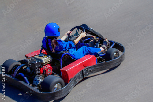 Karting on racing round in the open air. Woman behind the wheel of a kart. Girl rides on a kart with high speed.