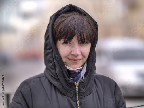 Portrait of a young woman in a hood on a city street, looking at the camera