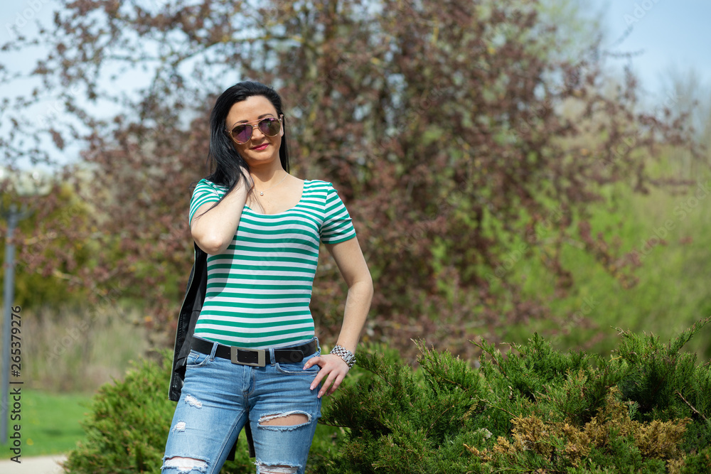 Brunette in sunglasses and black is standing and enjoying the sun in the park Brunette in sunglasses and black is standing and enjoying the sun in the park