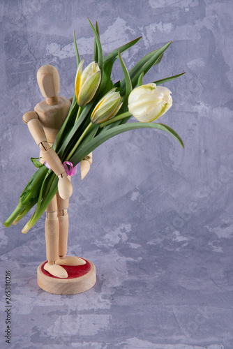 Wooden figure holding nice spring bouquet staying on grey background