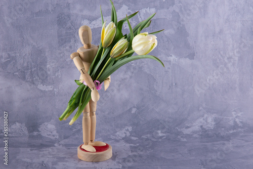 Wooden man figure staying on table, grey background and holding nice fresh spring bouquet of white tulips. Copy space for text