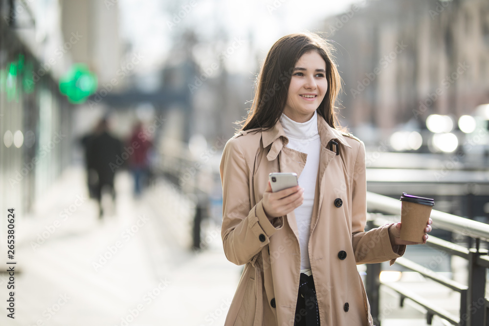 Young businesswoman checking email via mobile phone and holding a coffee cup against urban scene. Young businesswoman checking email via mobile phone and holding a coffee cup against urban scene.