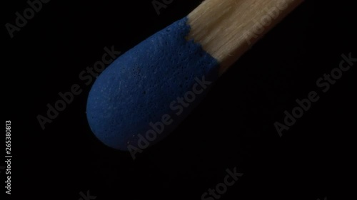 macro of blue matchstick igniting, burning and fuming in slowmotion on black background