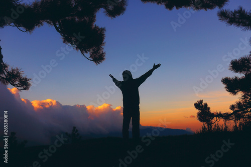  Silhouette of a man in the mountains at sunset, revealing hands in greeting and nature