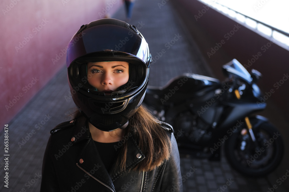 Attractive serious woman is standing next to her motobike. She is wearing a helmet. Attractive serious woman is standing next to her motobike. She is wearing a helmet.