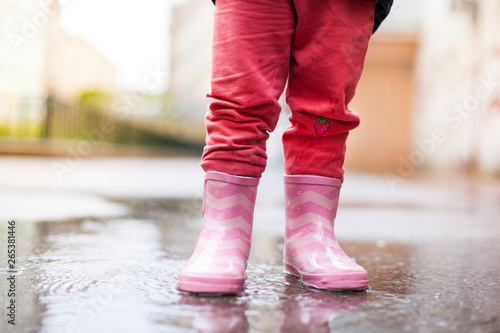 Kind steht mit rosa Gummistiefeln in Wasserpfütze. Child standing with pink rubber boots in puddle.