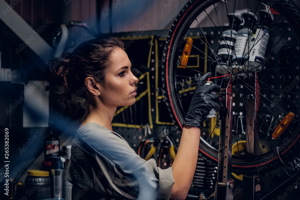 Young beautiful woman is repairing bicycle at busy workshop between pneumatic wires. Young beautiful woman is repairing bicycle at busy workshop between pneumatic wires.