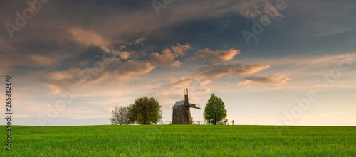 panorama of farm landscape with old wooden windmill under sunset clouds in Ukraine