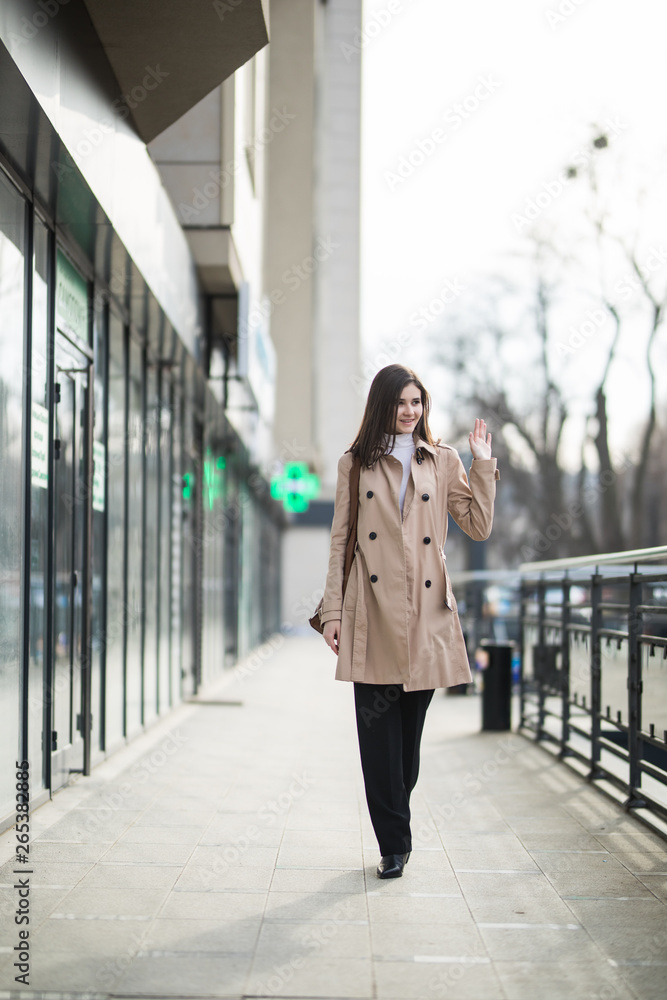Young woman walking on the street wearing stylish bright coat with handsbag