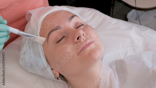Cleaning mask for a woman's face in the beauty salon. Doctor beautician puts moisturizing gel on the face with a brush.
