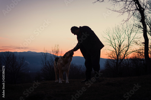 A silhouettes of a man and big dog and beautiful colorful sunset in mountains.
