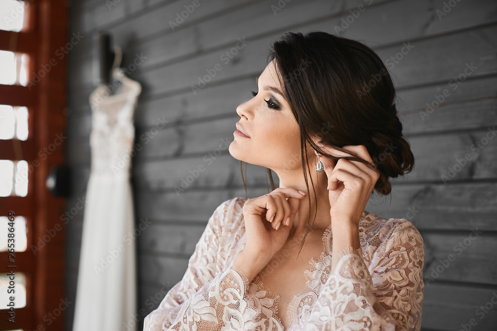Beautiful brunette model girl with wedding hairstyle and with professional makeup adjusting her earring, preparation for the wedding ceremony Beautiful brunette model girl with wedding hairstyle and with professional makeup adjusting her earring, preparation for the wedding ceremony