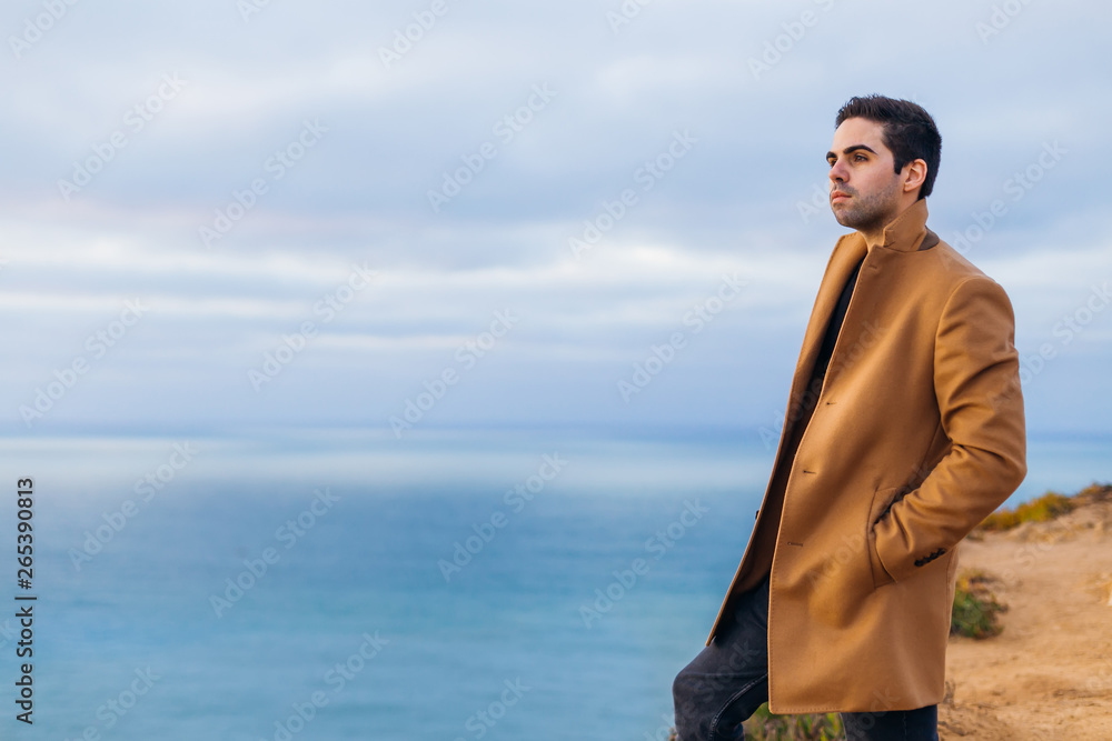 The guy holds his hands in his pockets in a beige coat standing The guy holds his hands in his pockets in a beige coat standing