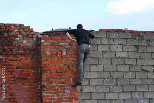 a man in dark clothes climbed onto an old brick fence and peeks over the wall photo