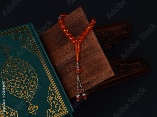 Islamic Holy Book Quran on wood carving rahle with rosary beads and prayer rug on black background. Kuran the holy book of Muslims. Ramadan concept. photo