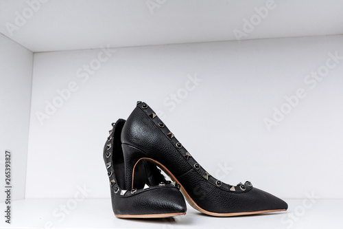 pair of black high-heeled shoes with pointed toes, decorated with metal inserts against a shelf in the store