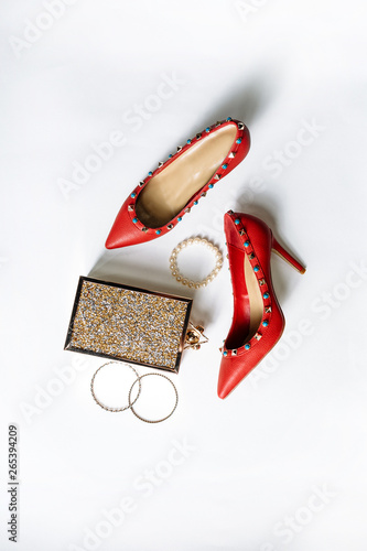 pair of red high-heeled shoes with pointed toes, decorated with metal blue inserts and metal clutch with sparcles on a white background