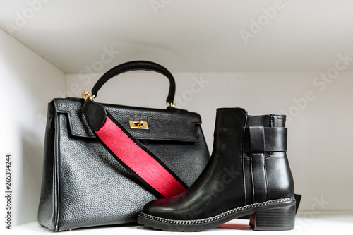 pair of black leather shoes with low heels and a black bag with a gold buckle and a red belt on a white shelf in the store