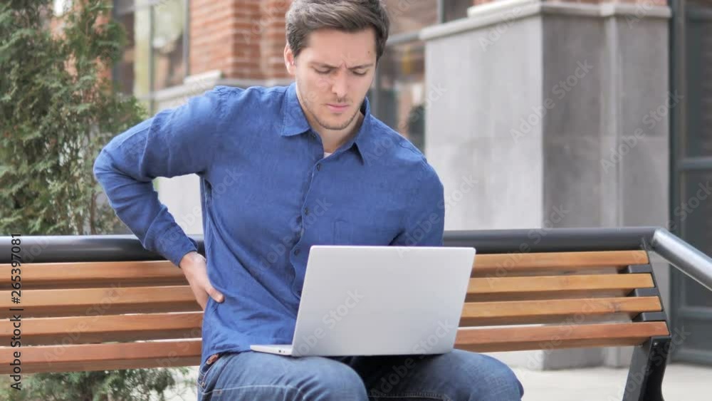 Sitting Outdoor Young Man with Back Pain Working on Laptop Sitting Outdoor Young Man with Back Pain Working on Laptop