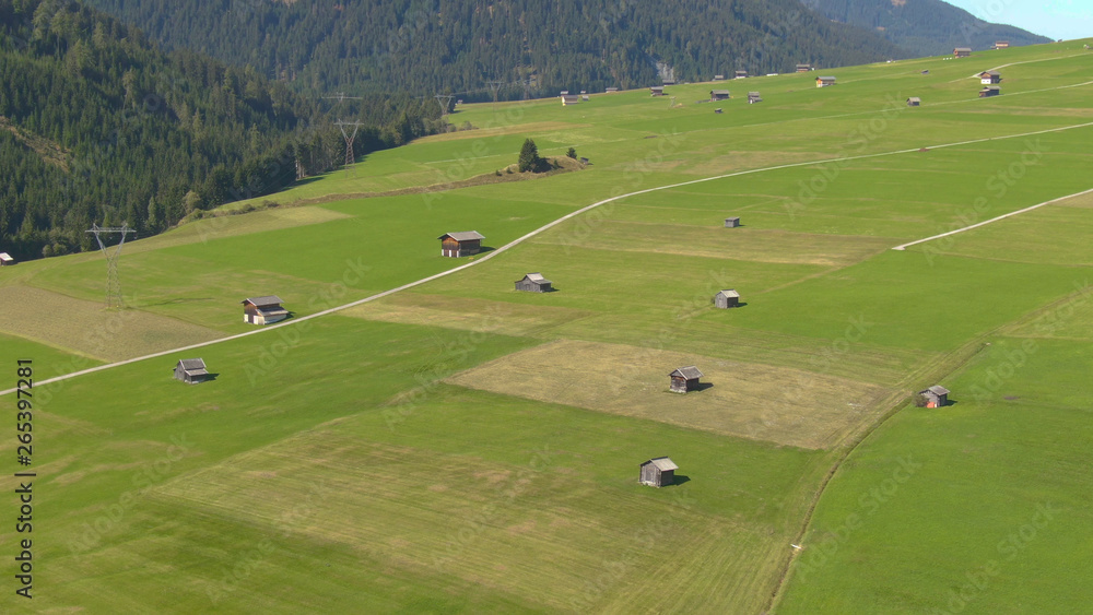 Naklejka premium AERIAL: Flying above wooden shacks scattered around the vibrant green meadows.