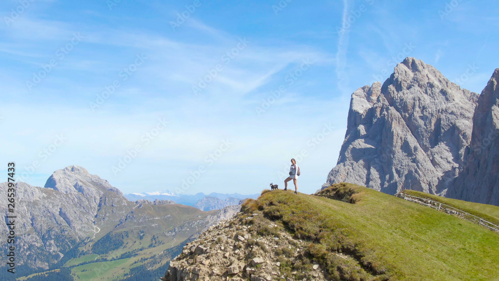 Obraz premium AERIAL: Woman observing the picturesque mountain landscape with her little dog.
