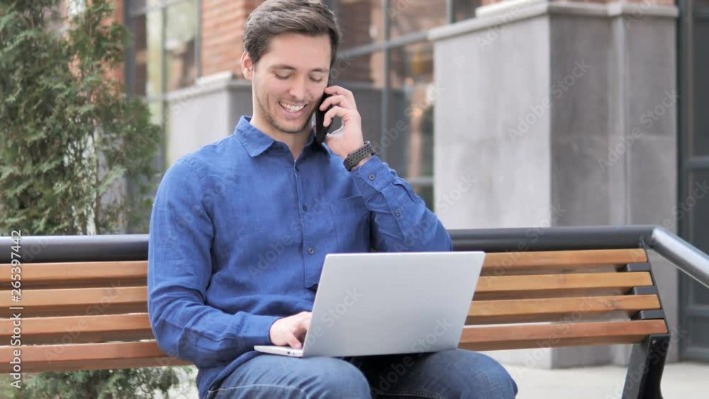 Working Young Man Talking on Phone, Sitting on Bench Working Young Man Talking on Phone, Sitting on Bench