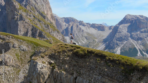 DRONE: Female hiker and puppy walk along the edge of a cliff in the Italian Alps