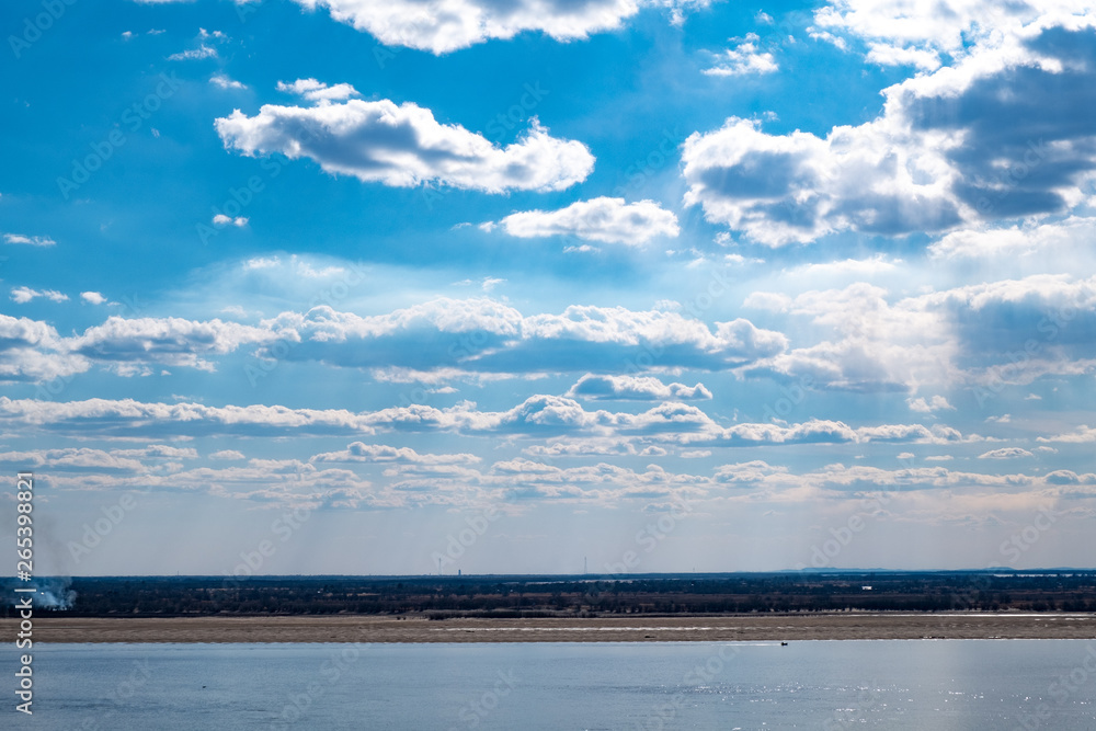 View of the Amur river against the blue sky with white beautiful clouds. Bright spring sun. Russia, Khabarovsk.
