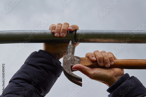 Using a hammer with women's hands to nail an aluminum bar. Grey sky background.