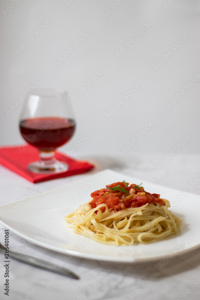 Pasta with fresh tomatoes, cooked with olive oil and garlic on a light background and a white square plate. Italian food. Vertical orientation Pasta with fresh tomatoes, cooked with olive oil and garlic on a light background and a white square plate. Italian food. Vertical orientation
