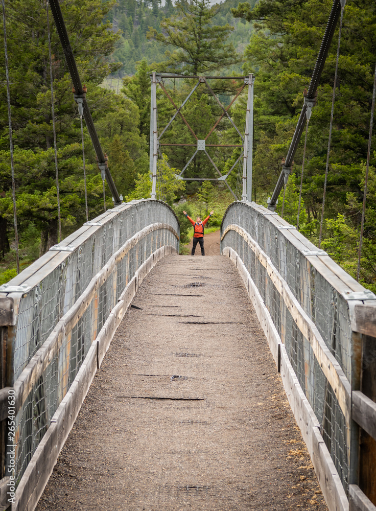 Obraz premium Man Holds up Arms Across Suspension Bridge