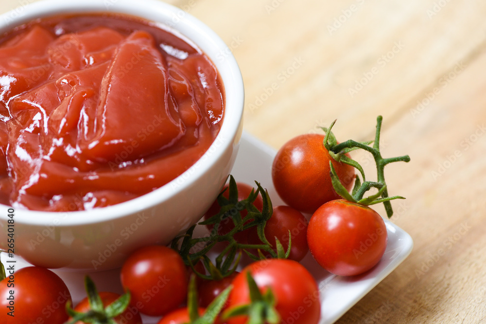 Ketchup in cup and fresh tomatoes on white plate Ketchup in cup and fresh tomatoes on white plate