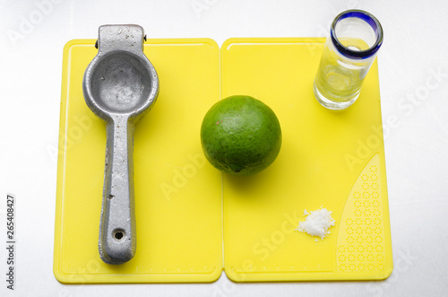Squeezer, lemon, salt and tequila shot glass on a yellow cooking table