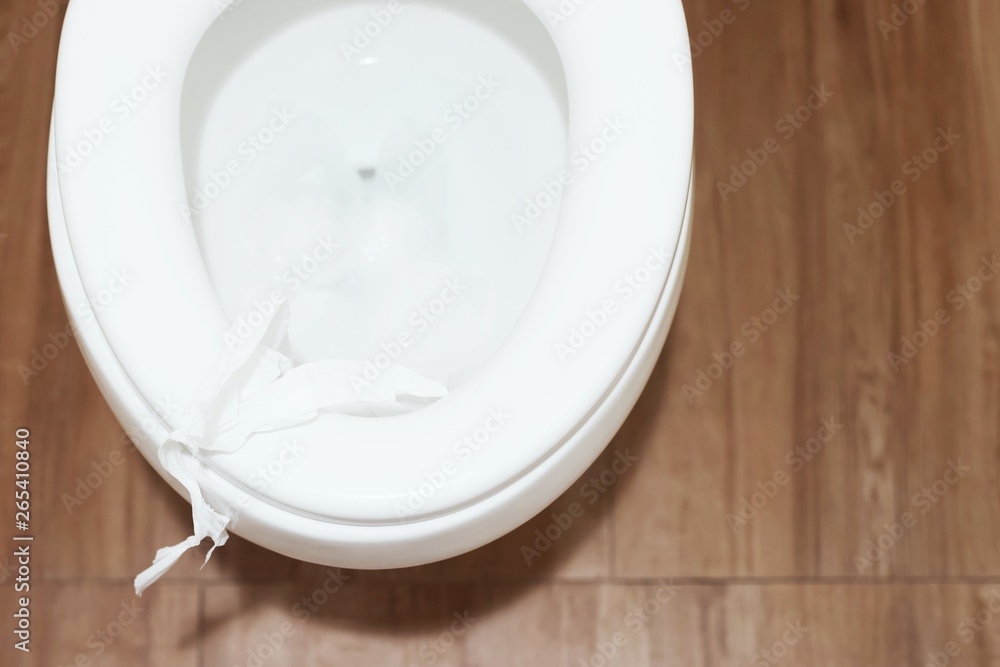 close up hand holding a tissue to be thrown into the toilet bowl. Can not drain water of toilet paper in the toilet bowl cause the stool to clog up. close up hand holding a tissue to be thrown into the toilet bowl. Can not drain water of toilet paper in the toilet bowl cause the stool to clog up.