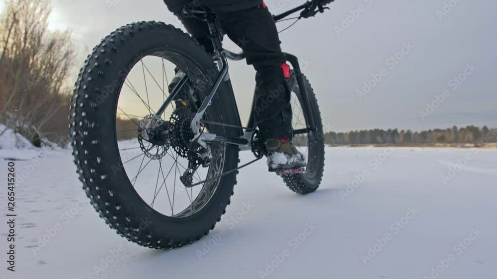 Professional extreme sportsman biker riding fat bike in outdoors. Close-up view of rear wheel. Cyclist ride in winter forest. Man on mountain bicycle with big tire. Snow fly into the lens camera. Professional extreme sportsman biker riding fat bike in outdoors. Close-up view of rear wheel. Cyclist ride in winter forest. Man on mountain bicycle with big tire. Snow fly into the lens camera.