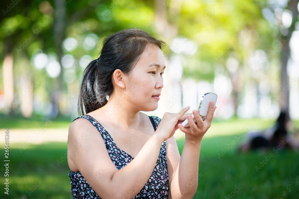 Beautiful Asian woman applying soft powder make up on her face in the park Beautiful Asian woman applying soft powder make up on her face in the park
