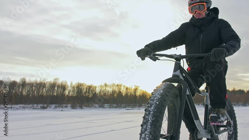 Professional extreme sportsman biker riding fat bike in outdoors. Cyclist ride in winter on snow ice. Man does trick on mountain bicycle with big tire in helmet and glasses. Slow motion in 180fps. photo