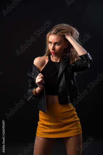 Wallpaper Mural Young beautiful woman wearing in a black leather jacket, black top, short skirt and boots  posing over black background. Studio shot of  blonde woman against black background Torontodigital.ca