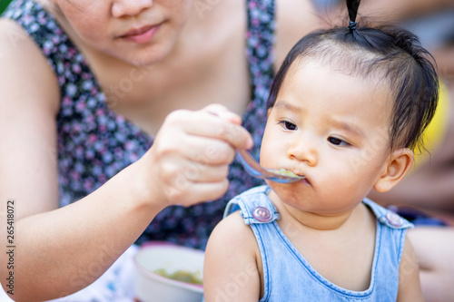 Asian woman feeding her baby girl by spoon