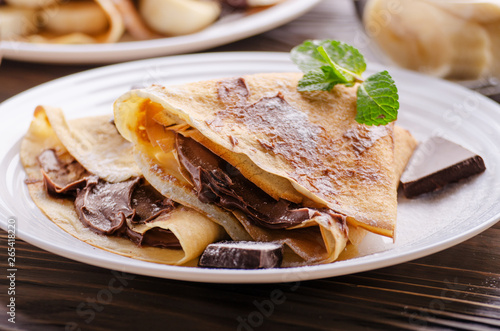 French crepes with chocolate sauce and banana in ceramic dish on wooden kitchen table photo