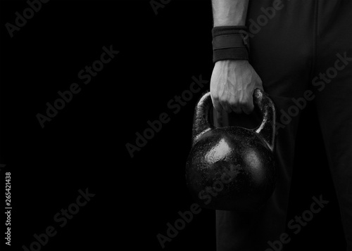 Close-up of a muscular hand holding a kettlebell. Kettlebell on a black background. The fist of an athlete clutching kettlebell.